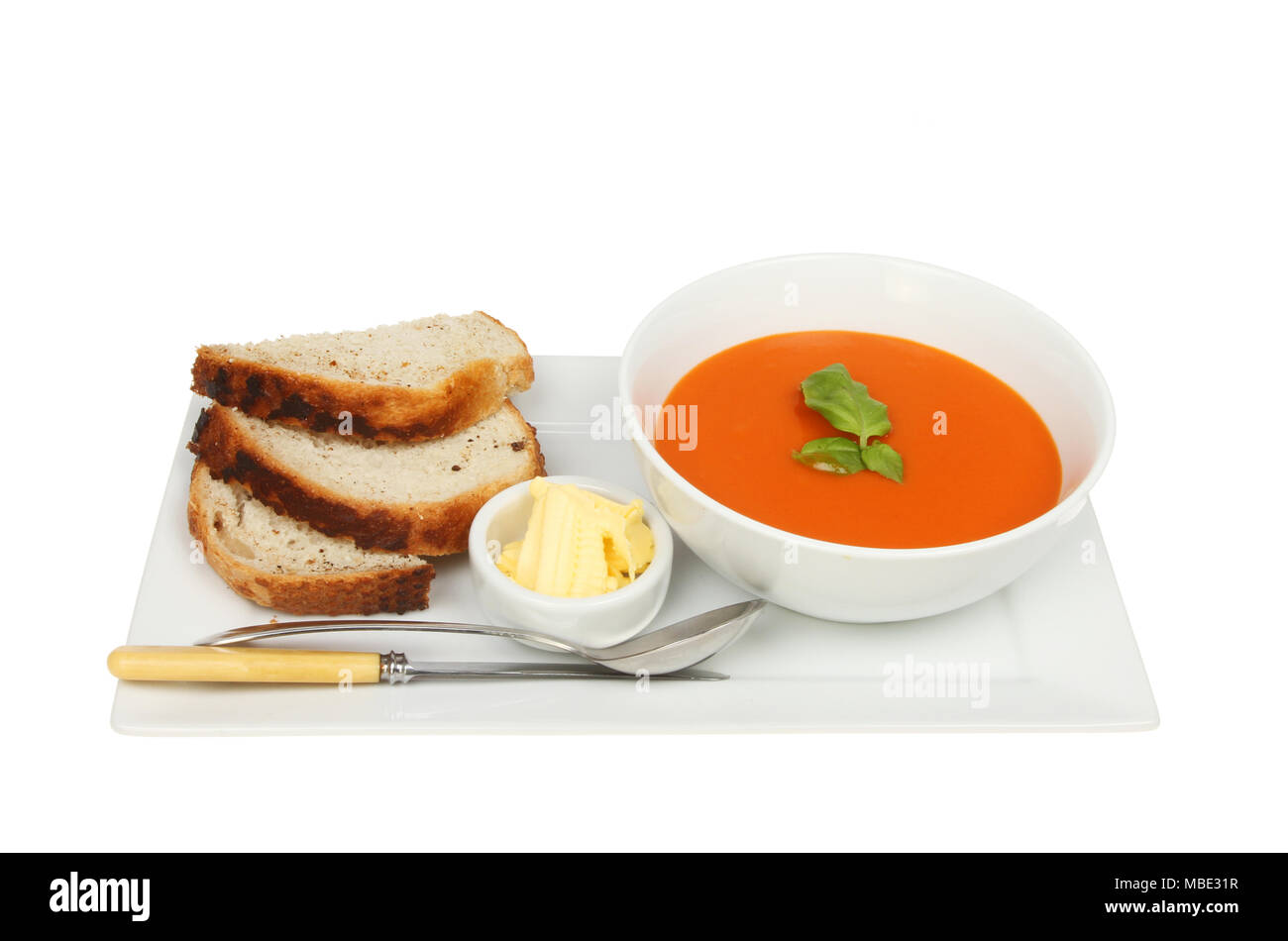 Schüssel mit Tomatensuppe mit Brot, Butter, Messer und Löffel Suppe auf einer rechteckigen Platte gegen Weiße isoliert Stockfoto