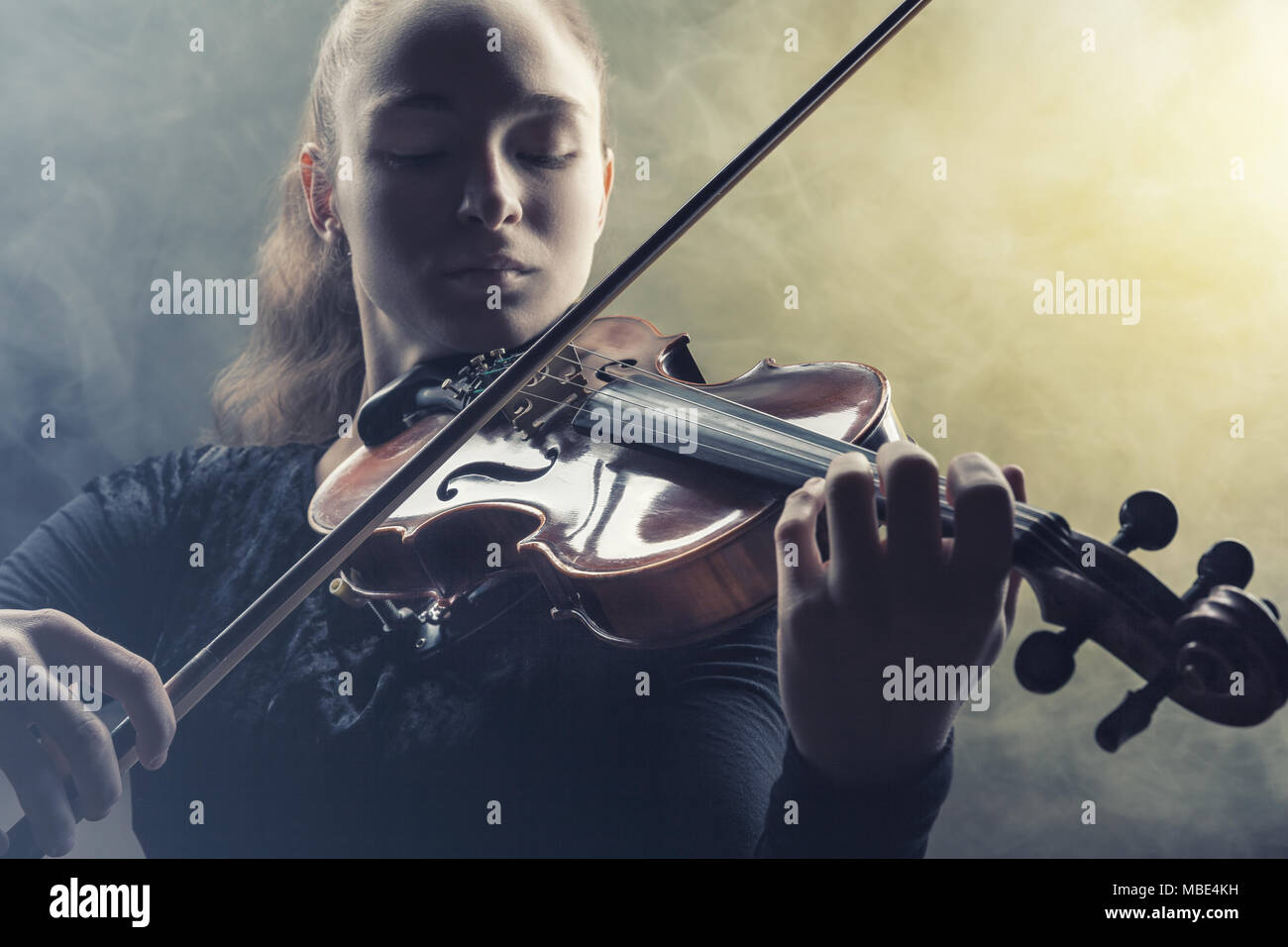 Frau Spielen der Violine vor einem dunklen Hintergrund. Nebel im Hintergrund. Studio shot Stockfoto