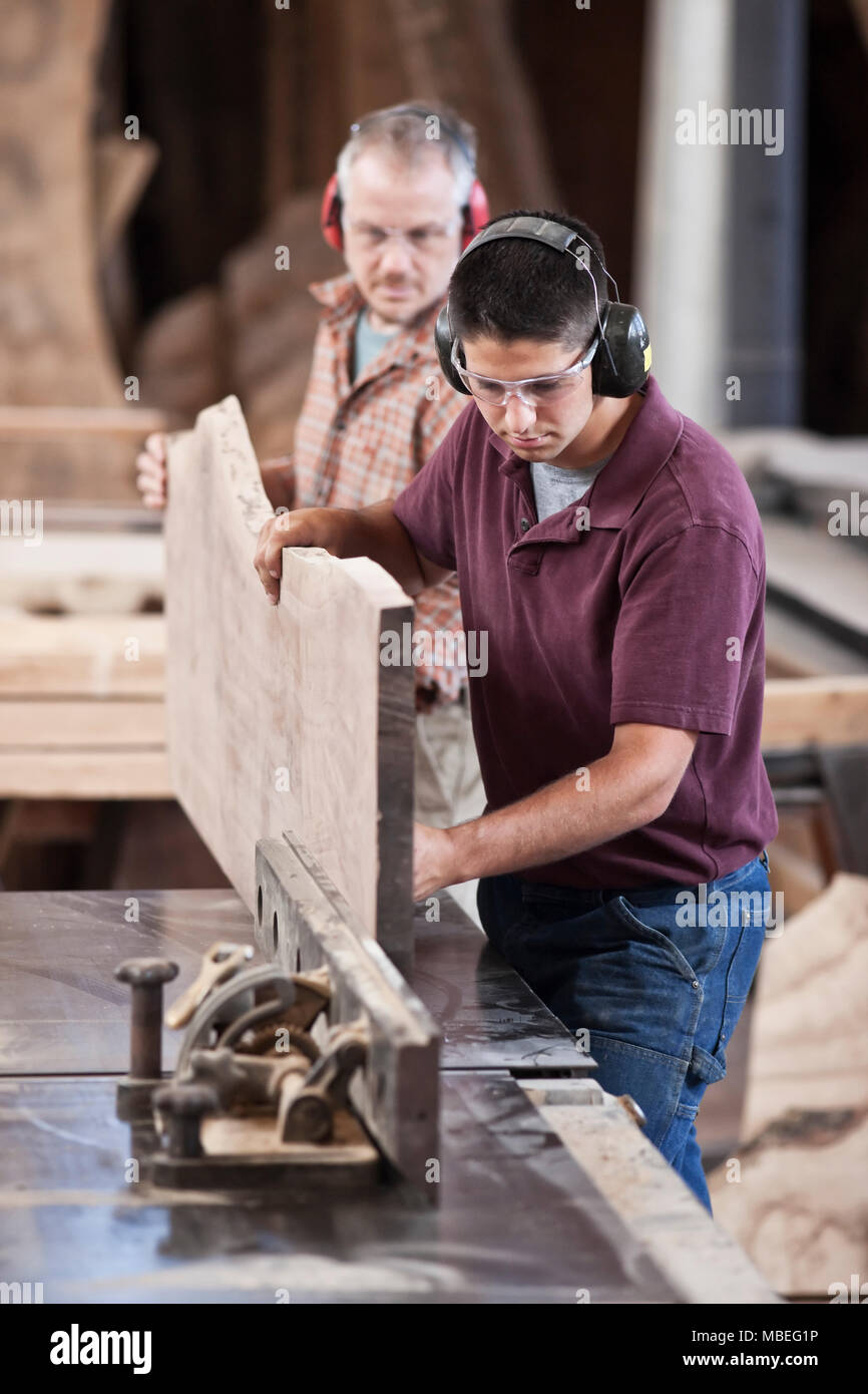 Team von zwei kaukasischen Männern schneiden eine große hölzerne Tafel auf einem Tisch sah in einem Holz verarbeitenden Fabrik. Stockfoto