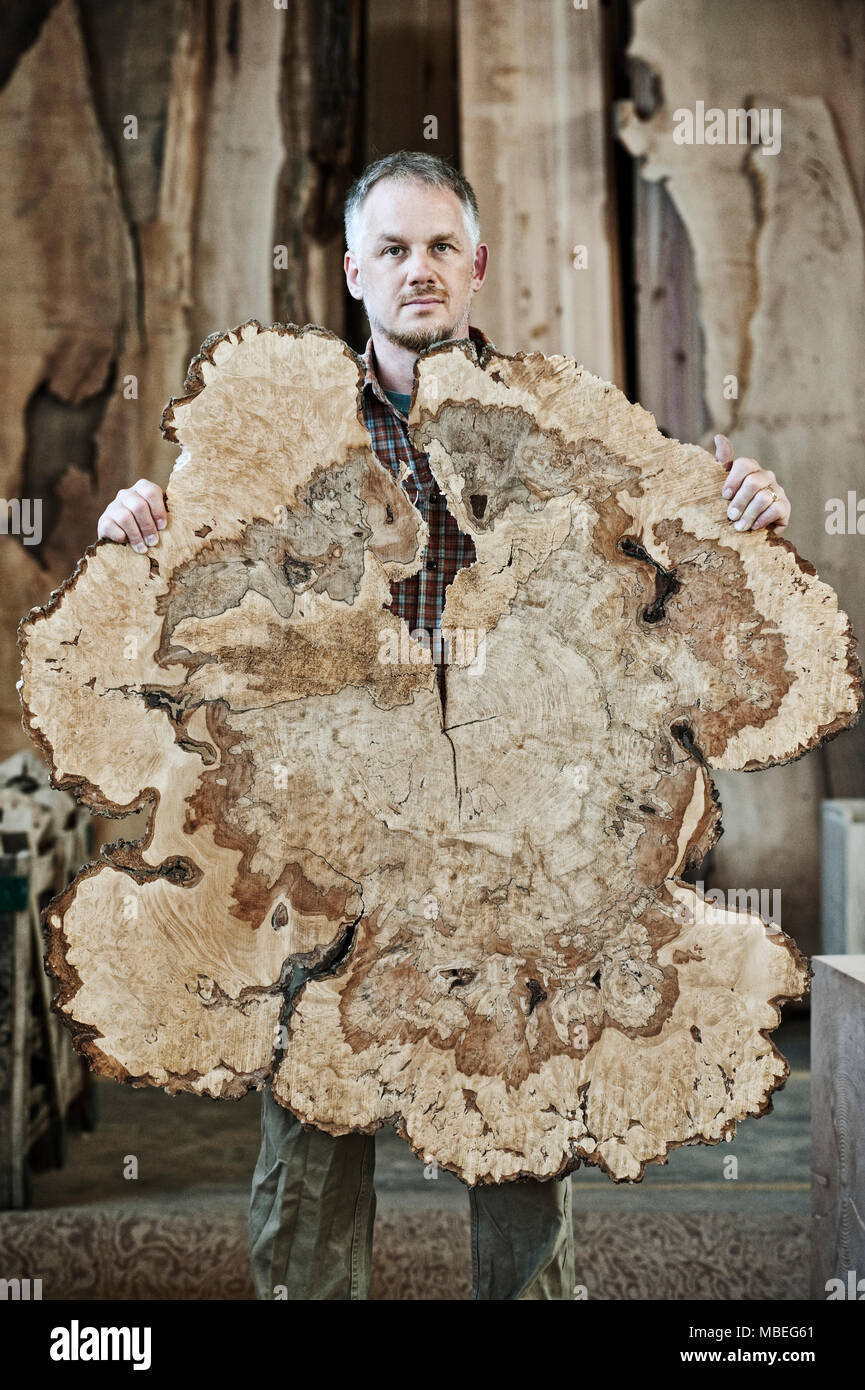 Kaukasische mann Arbeiter, der Holding der gesägt Querschnitt durch einen Baumstamm in einer Holz verarbeitenden Fabrik mit recyceltem Holz. Stockfoto