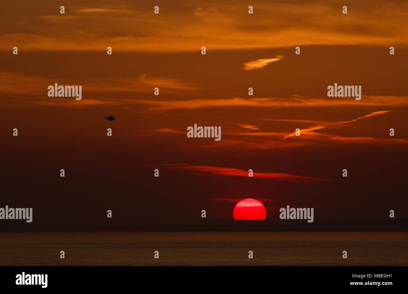 Roter Himmel und Sonne über den Solent mit dem Hubschrauber der Küstenwache zurück zur Basis nach einer Rettung rufen Stockfoto