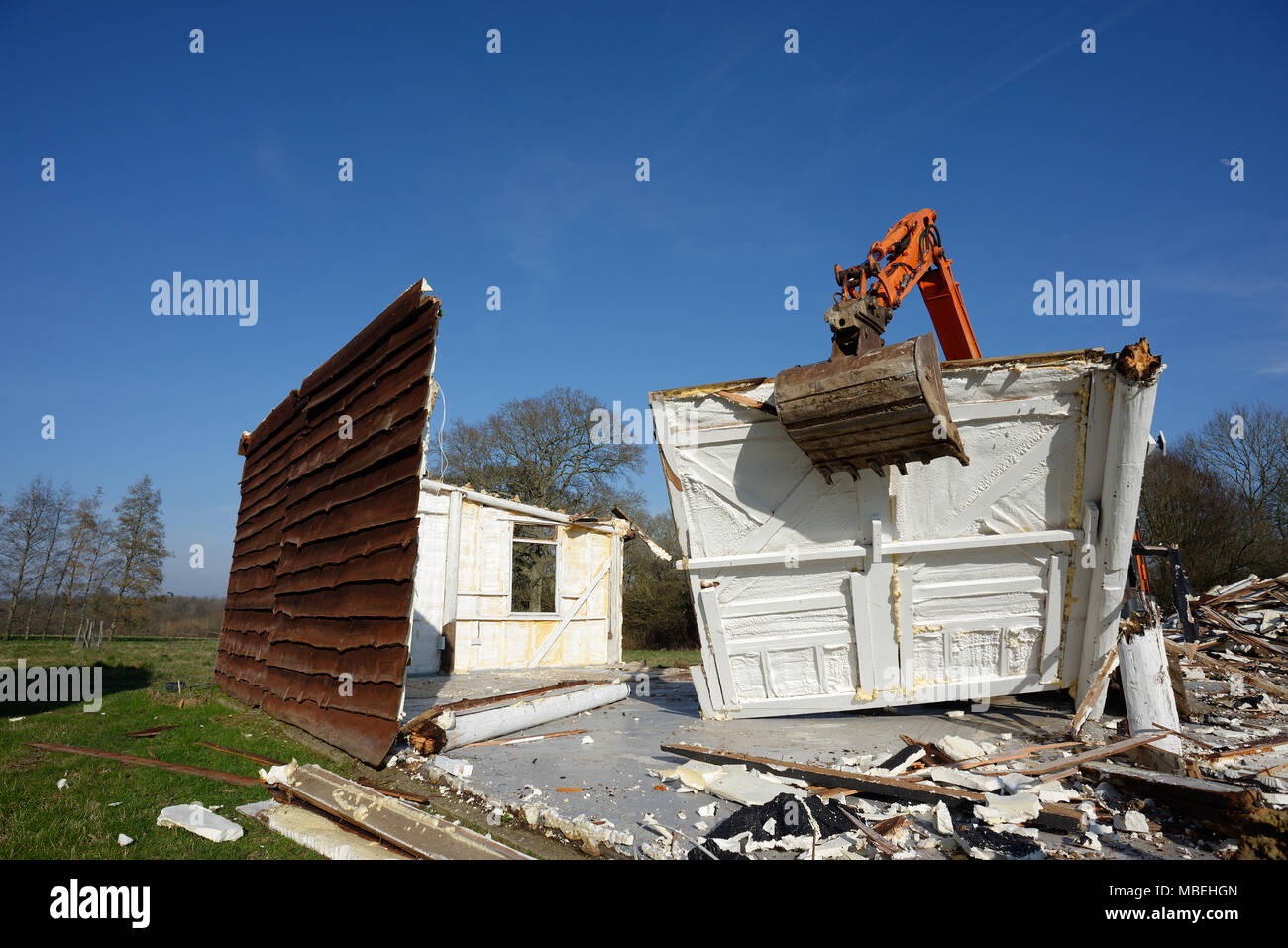 Ein großer Bagger verwendet eine Alte hölzerne Scheune zu demolieren. Stockfoto