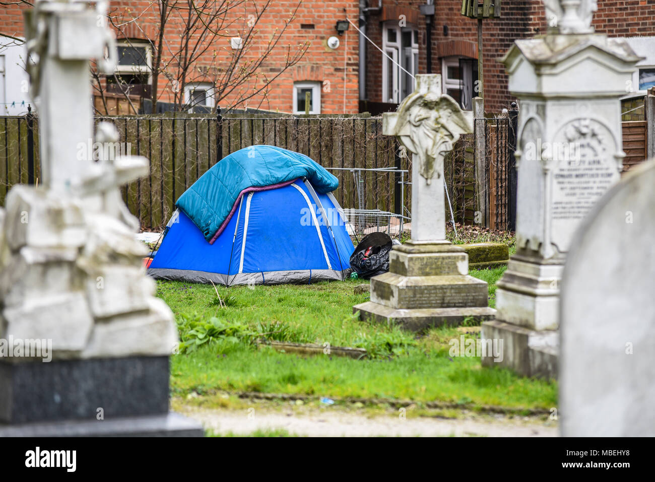 Obdachloser, der in einem Zelt auf einem Kirchenfriedhof mit Grabsteinen zeltet. Bettdecken über Leinwand. St. Johannes der Täufer Kirche Stockfoto