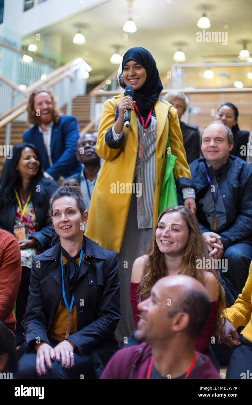 Lächelnde Frau im hijab im Gespräch mit Mikrofon in Konferenz Publikum Stockfoto
