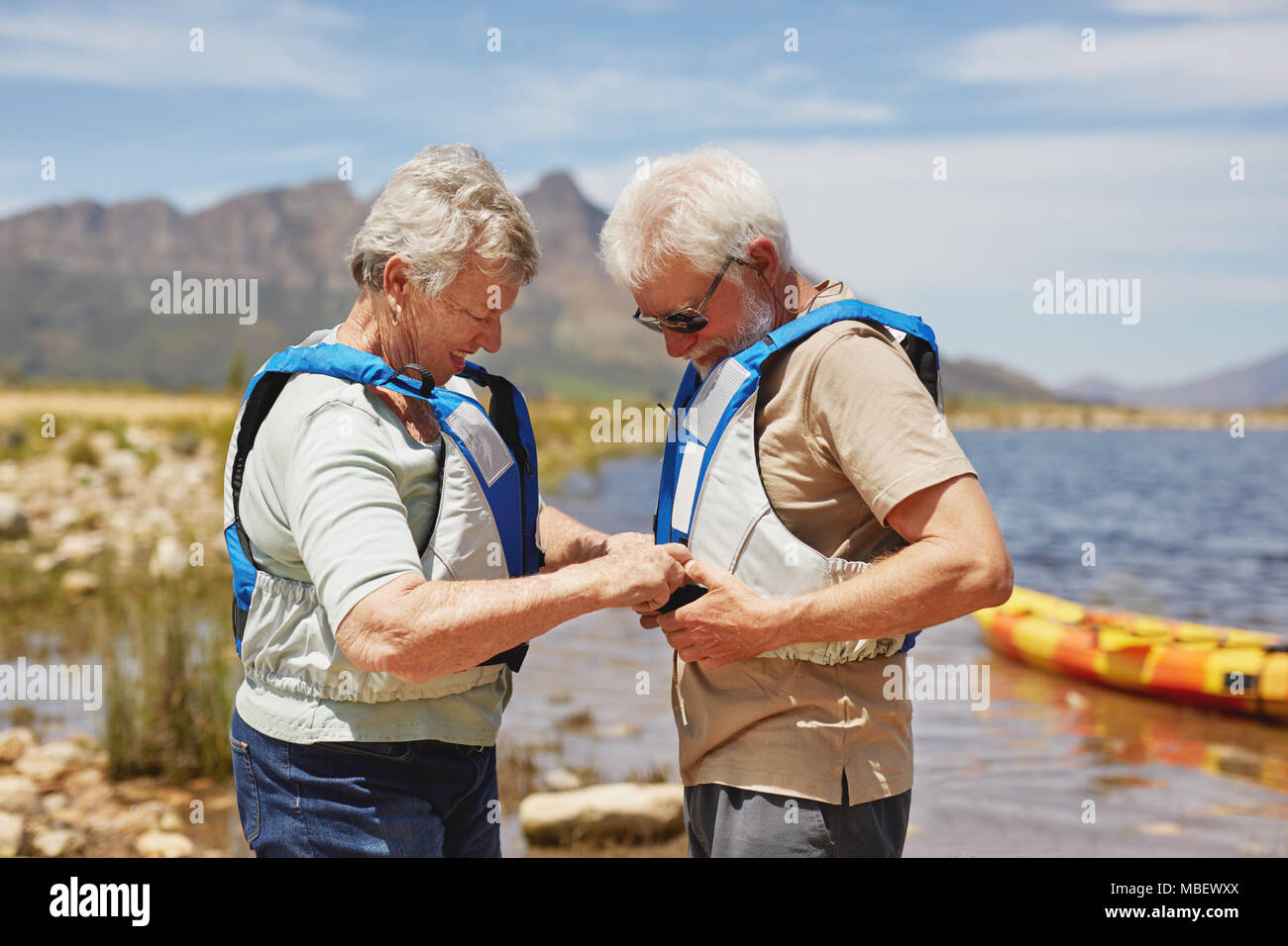 Active Senior Paar setzen auf Schwimmwesten, Vorbereitung für das Kajakfahren im sonnigen Sommer am See Stockfoto