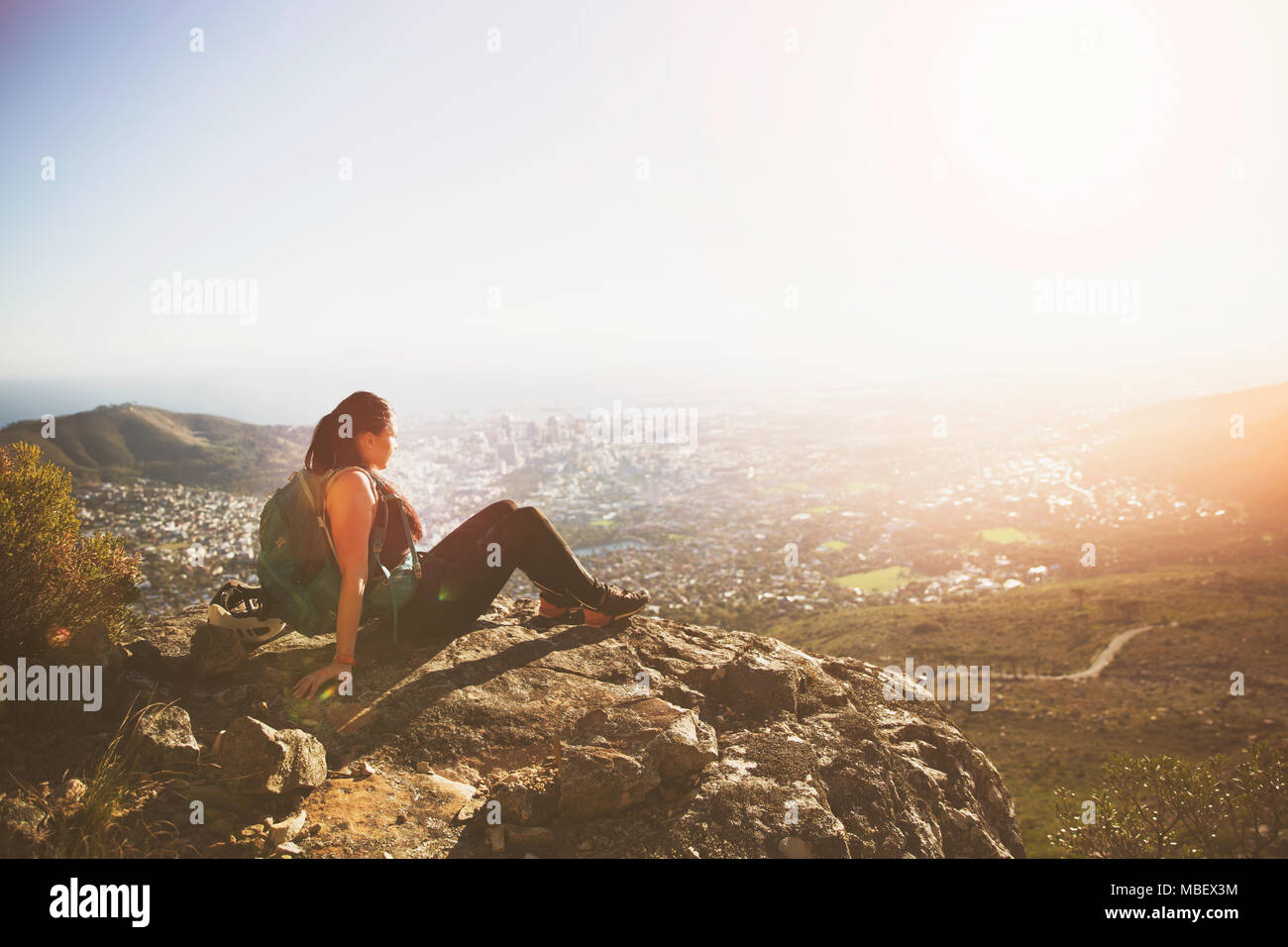 Serene weibliche Backpacker sitzen auf den Felsen über dem sonnigen Stadt Stockfoto