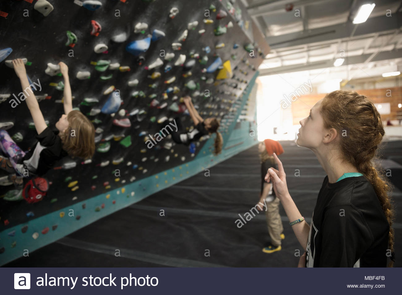 Neugierige Mädchen Kletterer beobachten Freund Kletterwand in der Kletterhalle Stockfoto
