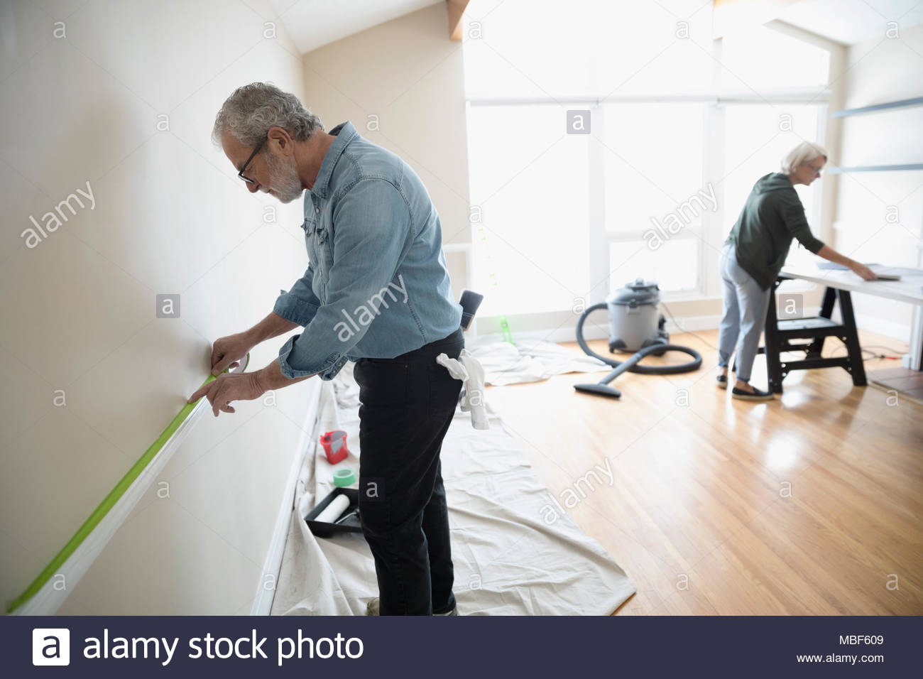 Älterer Mann taping, Vorbereitung Stuhl Schiene im Wohnzimmer zu malen, Do-it-Yourself Stockfoto