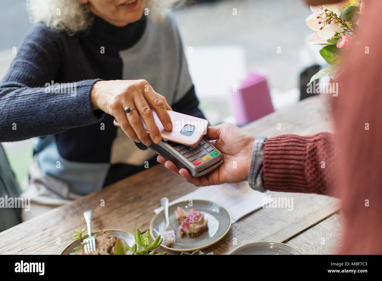 Frau mit smart phone über kontaktlose Zahlung im Cafe Stockfoto