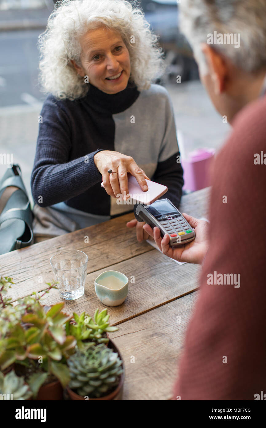 Frau mit smart phone kontaktloses Bezahlen im Café Stockfoto