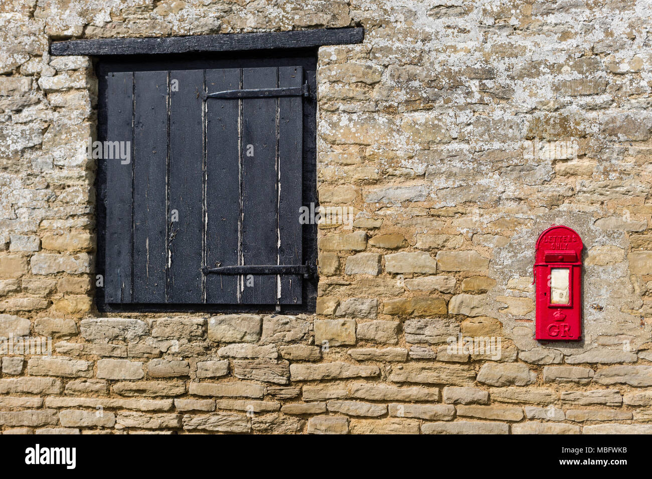 Alte Steinmauer mit einem schwenkbaren Holz- Fenster und einer alten roten Briefkasten inset; Ravenstone, Buckinghamshire, Großbritannien Stockfoto