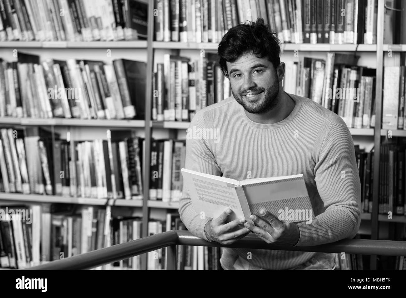 Stattlicher Mann mit dunklen Haaren steht in der Bibliothek - Studentische Vorbereitung Prüfung und Lehren in der Schule Bibliothek Stockfoto