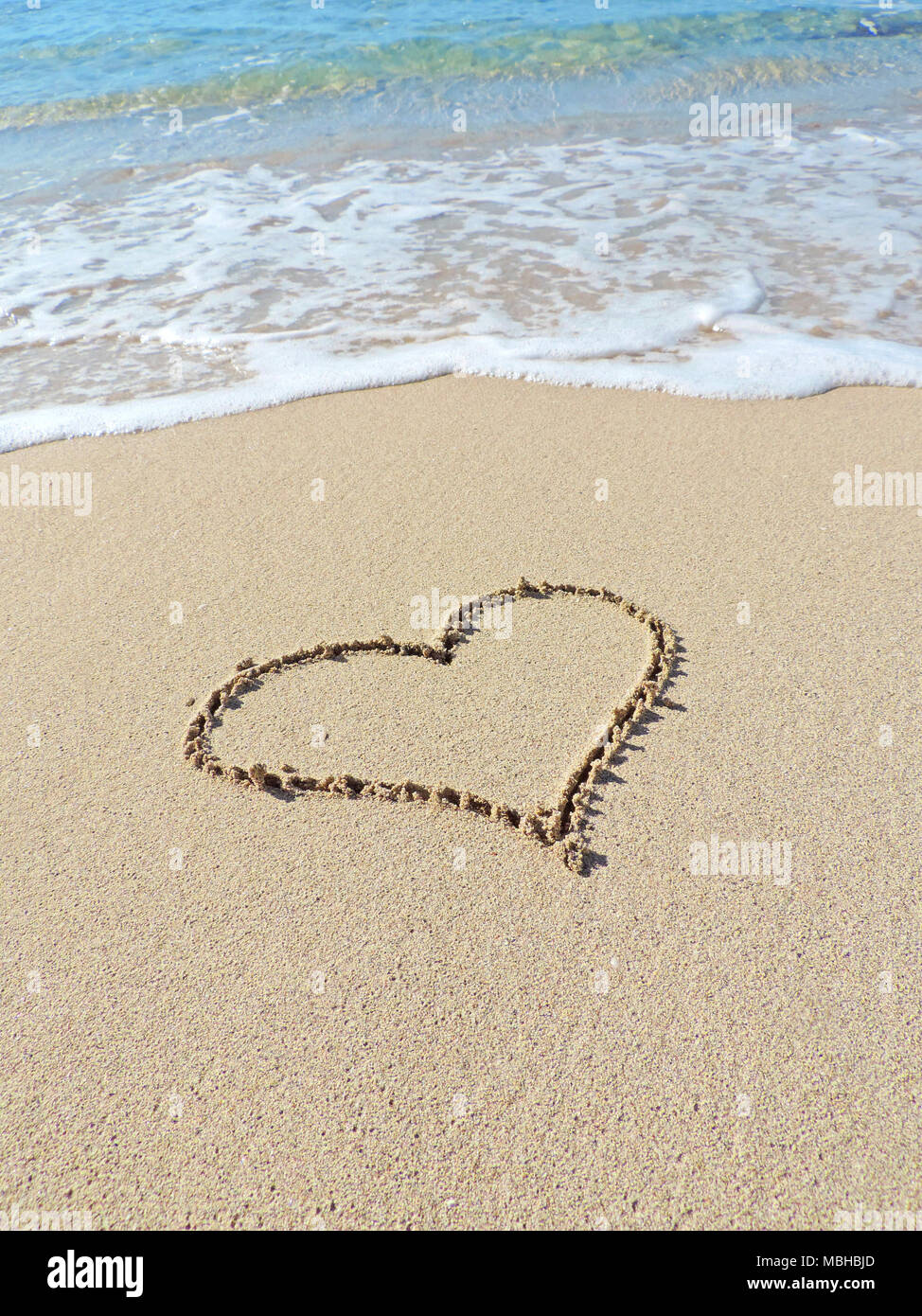 Herz Form, Zeichnung in der Sonne, Sommer Love theme. Das herzsymbol am Strand mit türkisblauem Meer und Sonne. Sommer Beach Szene. Stockfoto