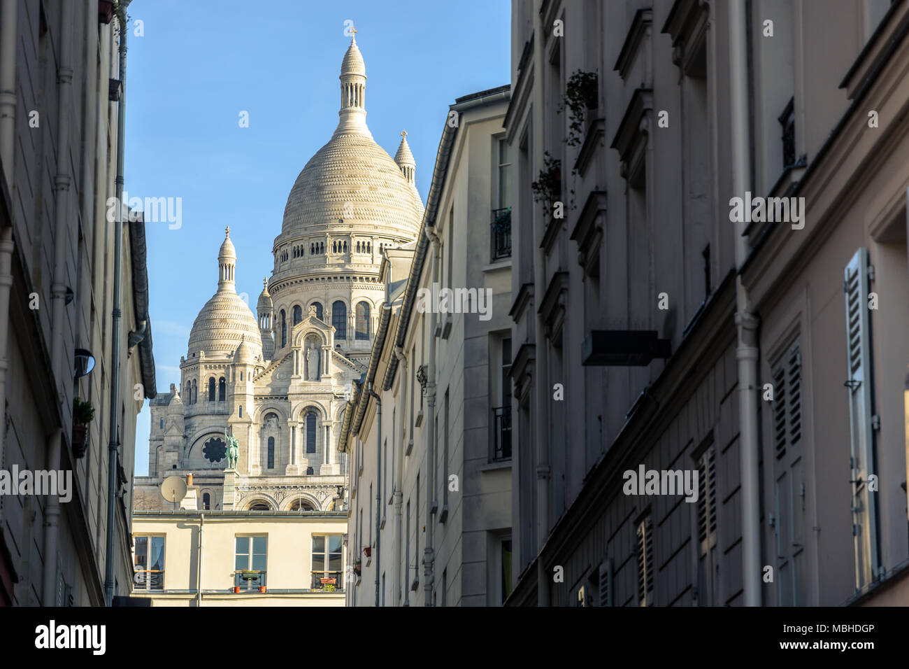 Blick auf die Fassade und die Kuppel der Basilika der Heiligen Herzen von Paris durch eine enge Straße zwischen alten Pariser Gebäude unter einem klaren blauen Himmel Stockfoto