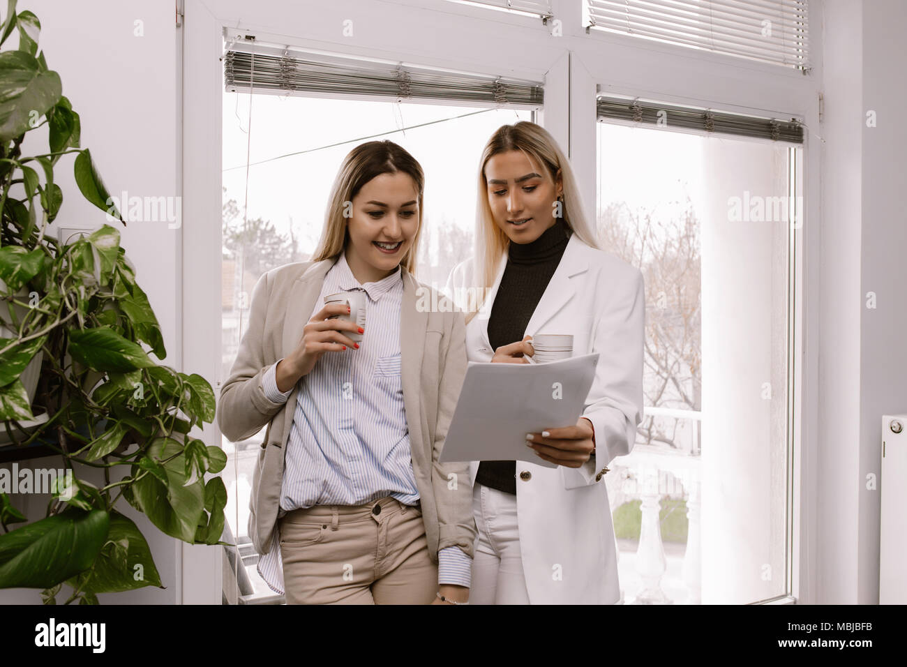 Zwei weibliche Kollegen nebeneinander stehen und diskutieren über die Arbeit beim Kaffee trinken in einem Büro. Stockfoto