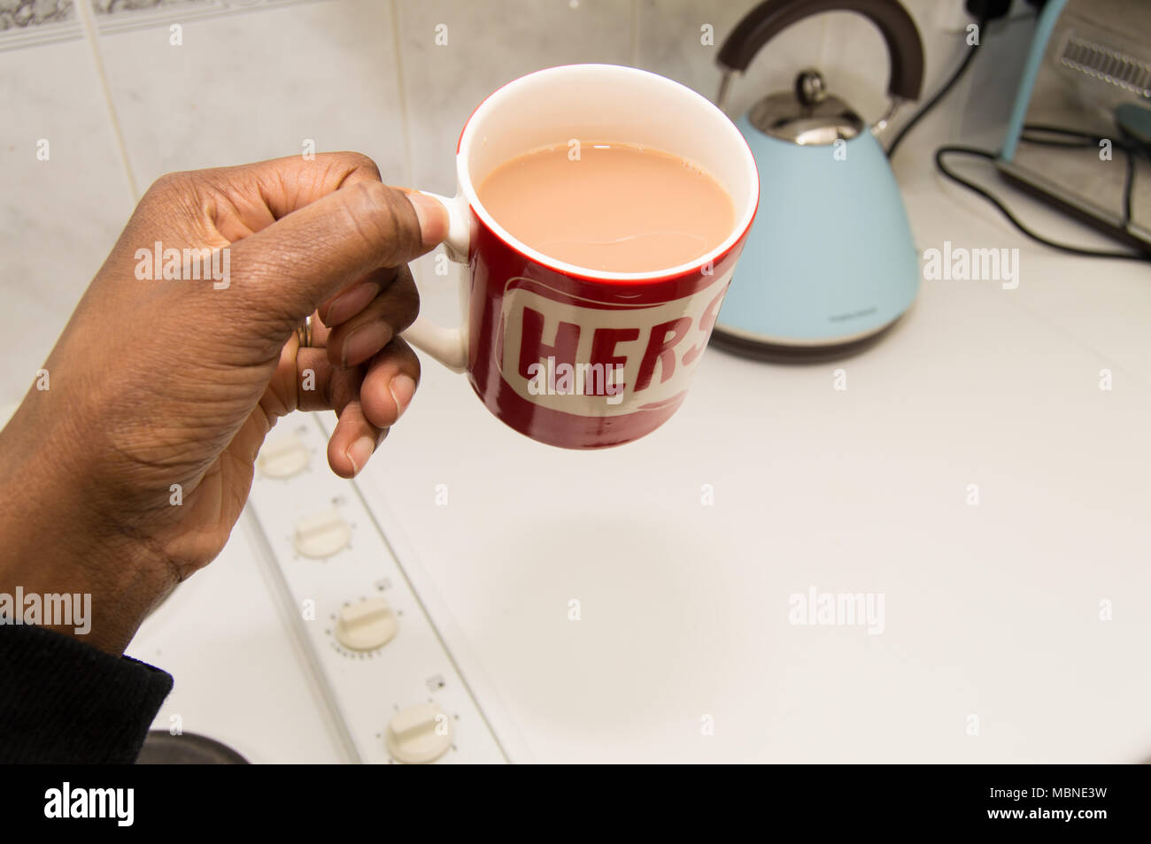 Erste Person Bild einer schwarzen Frau, die bei einer Tasse Tee mit einem blauen Wasserkocher Stockfoto