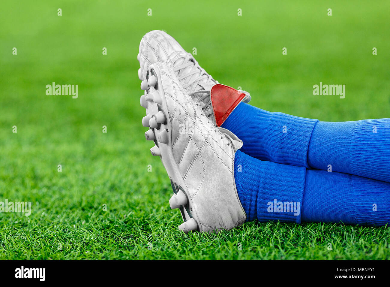 Beine von einem Spieler im Fußball, ein Athlet in blauen und weißen Manschetten mit Nieten Sneakers auf die grüne Wiese. Für die Inschrift, Ruhe, Pause, Timeout, Stockfoto