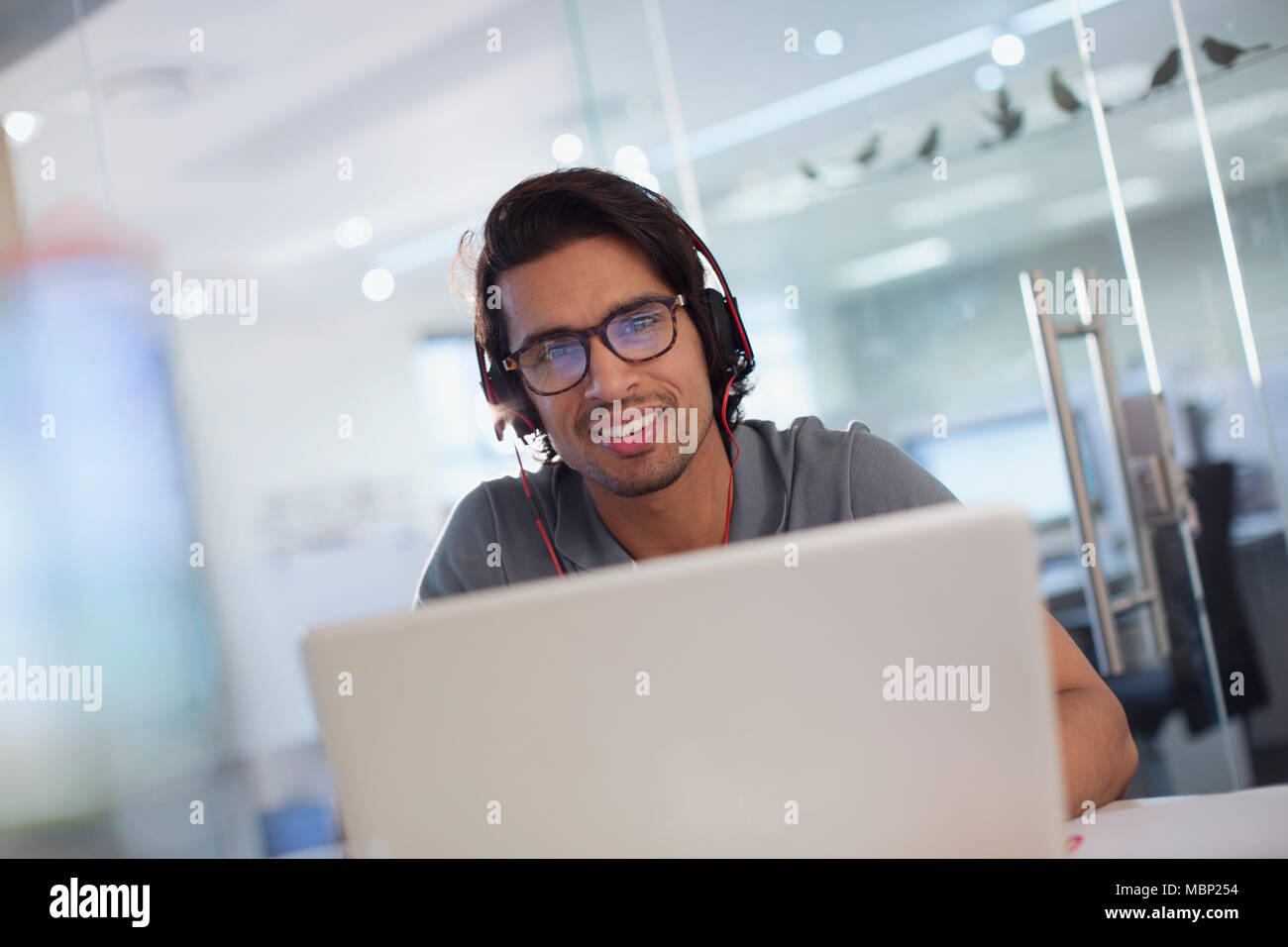 Porträt Lächeln, zuversichtlich, dass kreative Unternehmer mit Kopfhörern bei Laptop im Büro Stockfoto