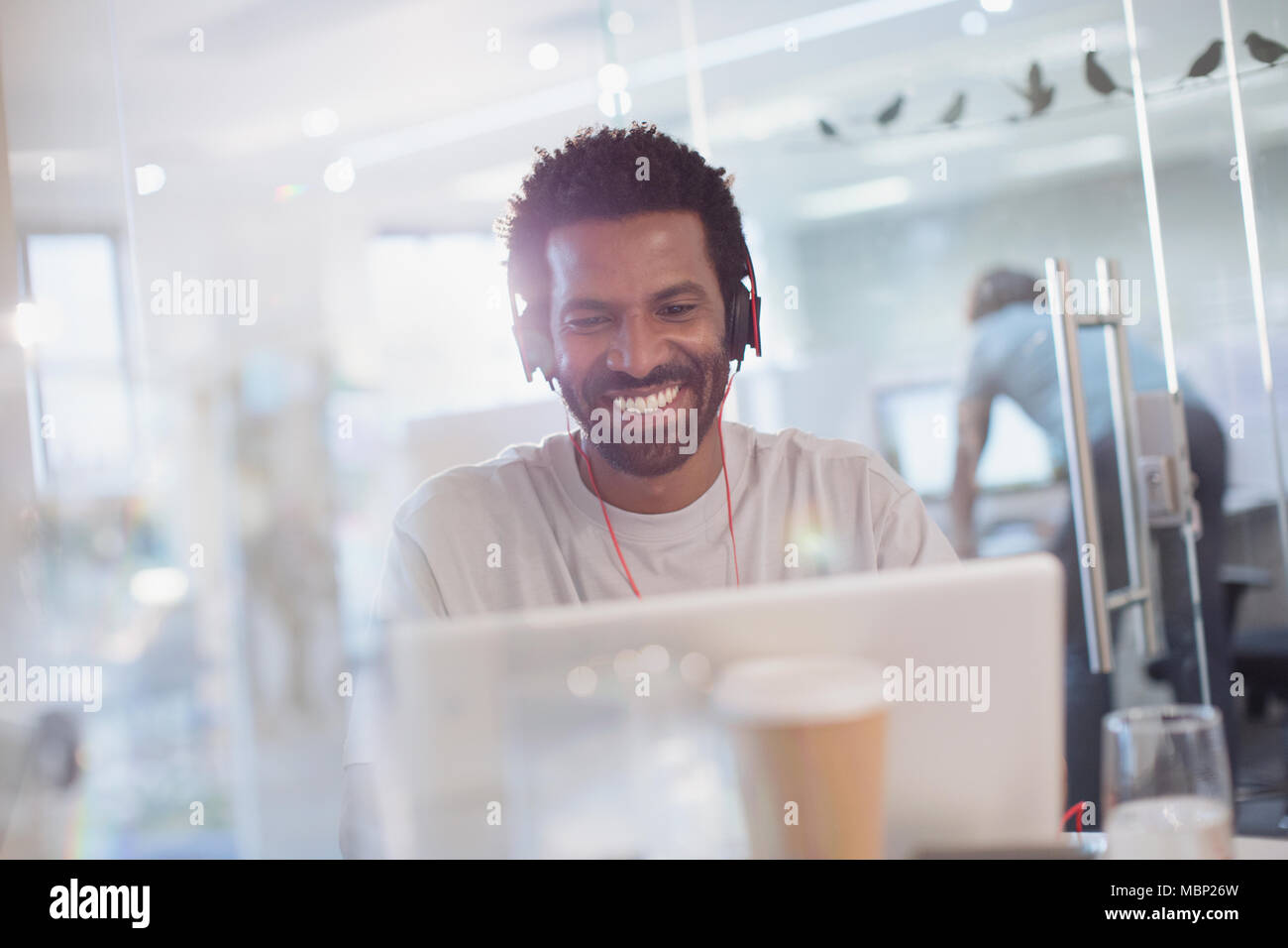 Lächelnd, zuversichtlich, dass kreative Unternehmer mit Kopfhörern mit Laptop im Büro Stockfoto