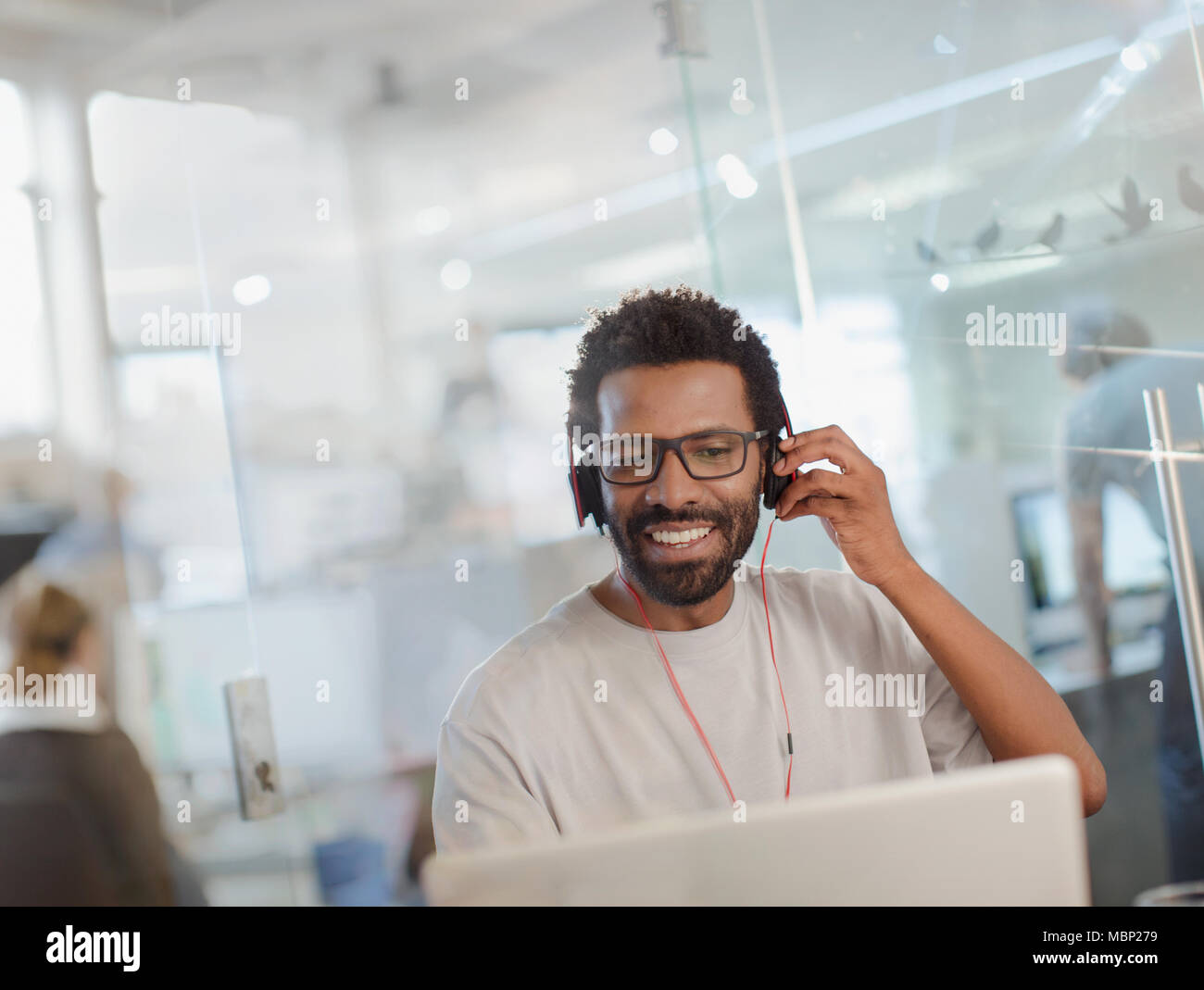 Lächelnde kreative Geschäftsmann mit Kopfhörern am Laptop arbeiten im Büro Stockfoto