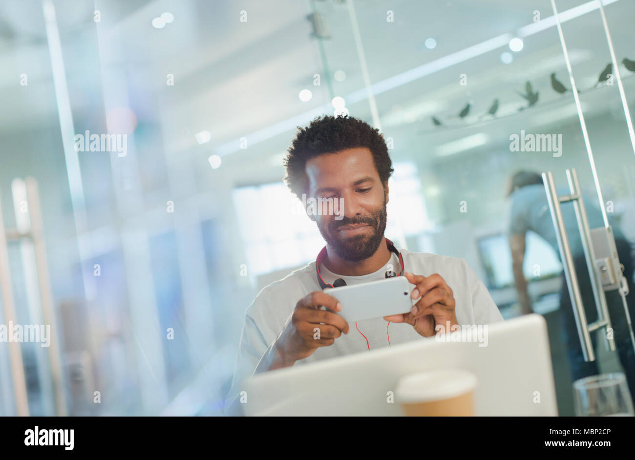 Lächelnde kreative Unternehmer mittels Smart Phone at laptop Stockfoto