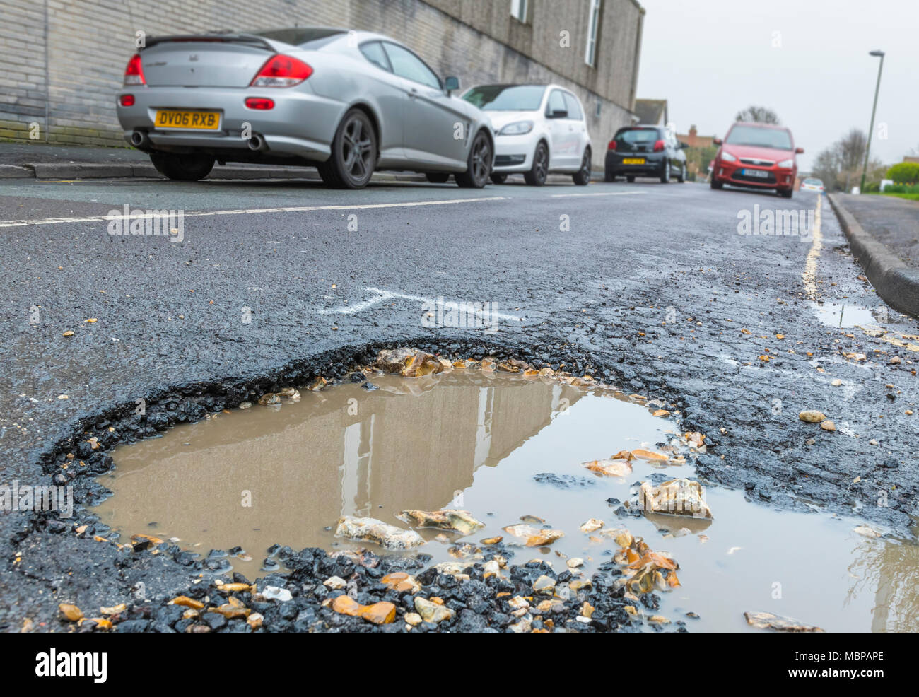 Schlagloch auf einer Asphaltstraße mit Regenwasser in England, Großbritannien. Beschädigte Fahrbahn. Straße, die sich in Not oder reparieren. Große Schlaglöcher. Sie auf das riesige Schlagloch. Stockfoto