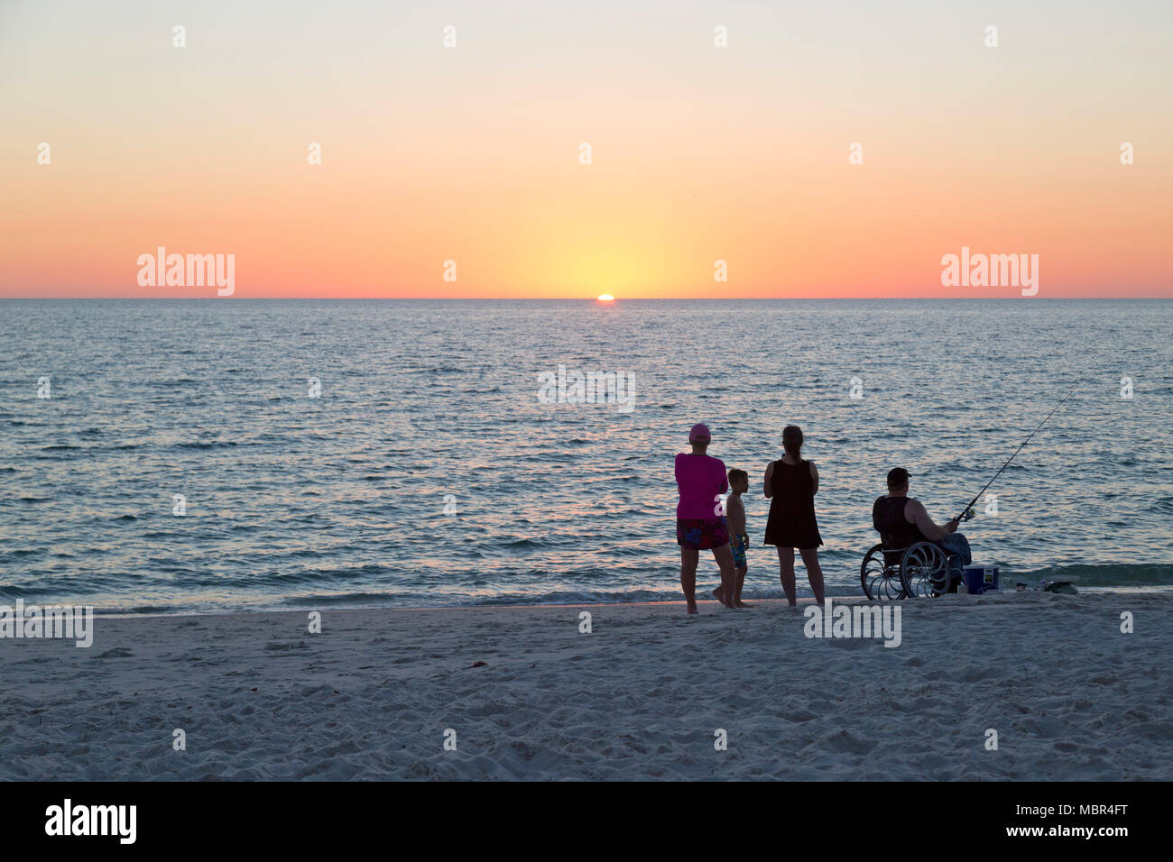 Familie am Strand bei Sonnenuntergang. Mann im Rollstuhl, Angeln. Stockfoto