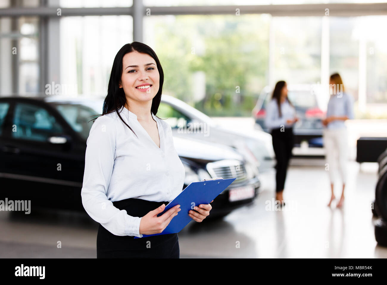 Die Frau, die im Autohaus mit ihren Kollegen im Hintergrund Stockfoto