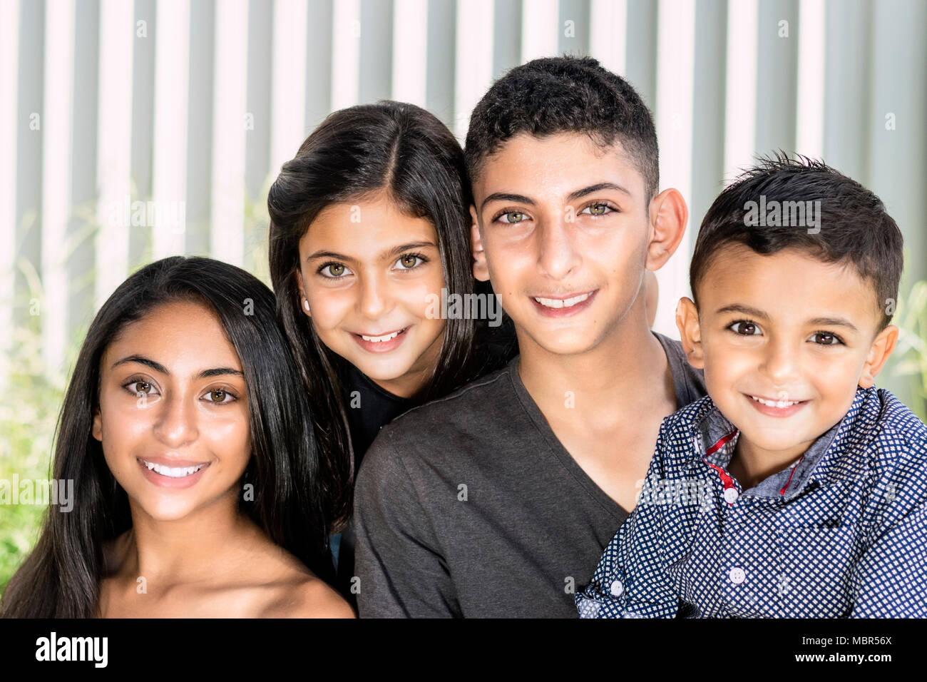 Lächelnd Geschwistern im Garten. Outdoor Portrait von zwei Brüder und zwei Schwestern, verschwommenes weiß Zaun Hintergrund. Stockfoto