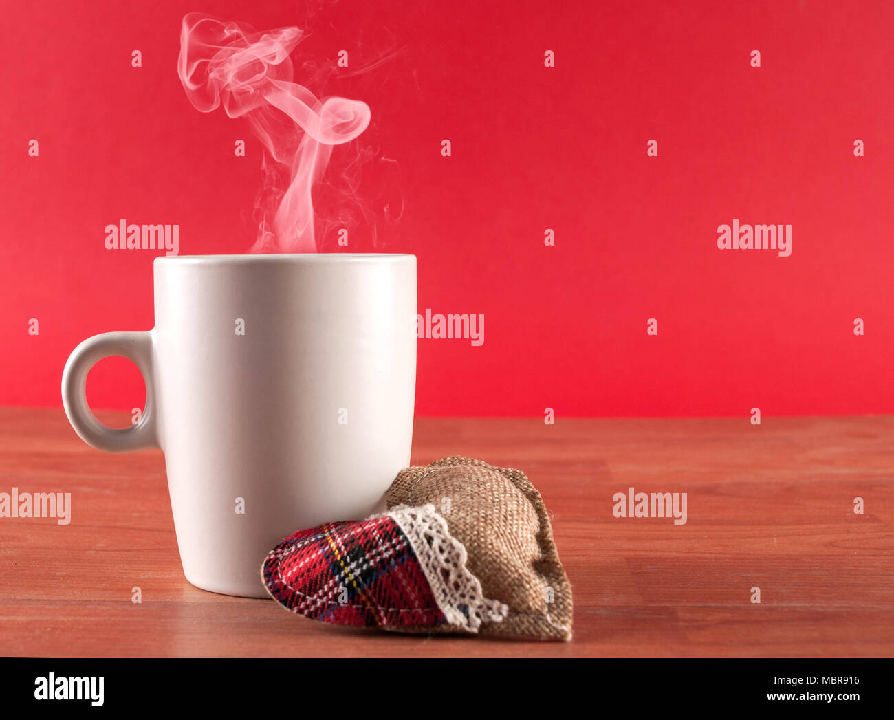 Tasse Kaffee mit Rauch und Herzen auf hölzernen Schreibtisch auf rotem Hintergrund. Valentinstag Konzept Stockfoto