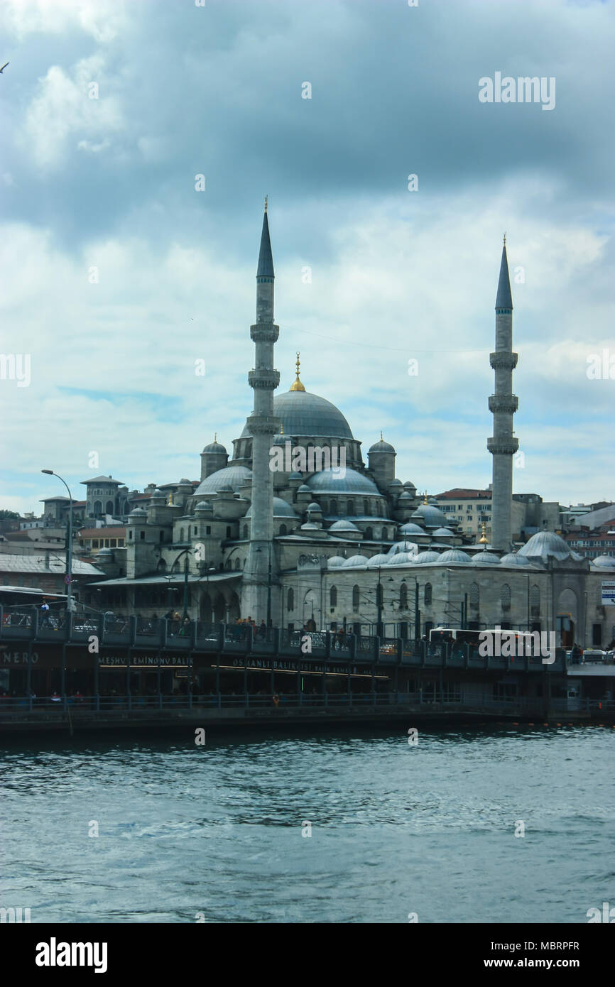 Schönen blauen Yeni Kami Moschee in Istanbul als von einer Fähre mit bewölktem Himmel und Istanbul City scape es Umgebung gesehen. Stockfoto