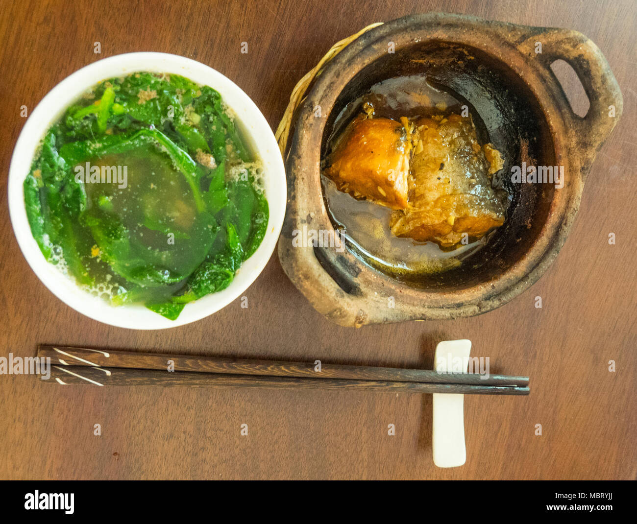 Ca Kho zu, eine geschmorte claypot von Wels oder basa Fisch und einer Schüssel grünem vegetavles, morning glory, rau Muong, oder Wasser Spinat, Ho Chi Minh City. Stockfoto