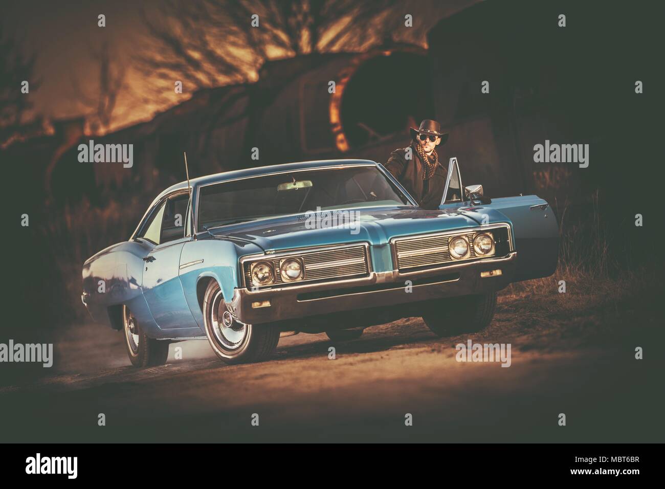 Classic Car Fahren. American Cowboy in westliche Kleidung Vorbereiten einer Fahrt in seinem American Classic Muscle Car während der malerischen Sonnenuntergang. Stockfoto