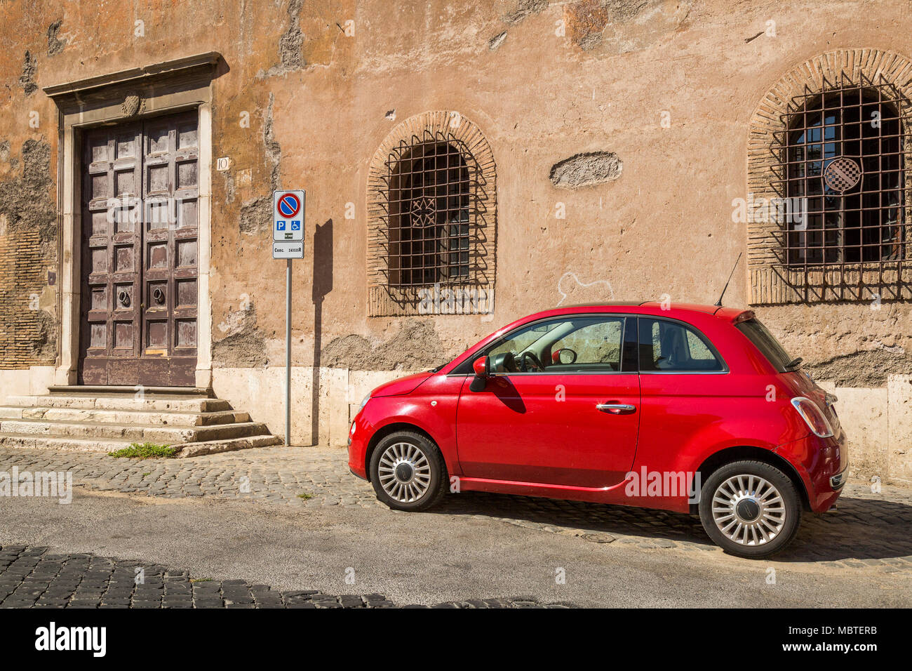 Ein roter Fiat 500 auf einer teilweise gepflasterten Straße im Stadtteil Trastevere in Rom, Italien, ist sie in einen behinderten Parkplatz geparkt, als durch die in der Nähe Vorzeichen dargestellt, Stockfoto