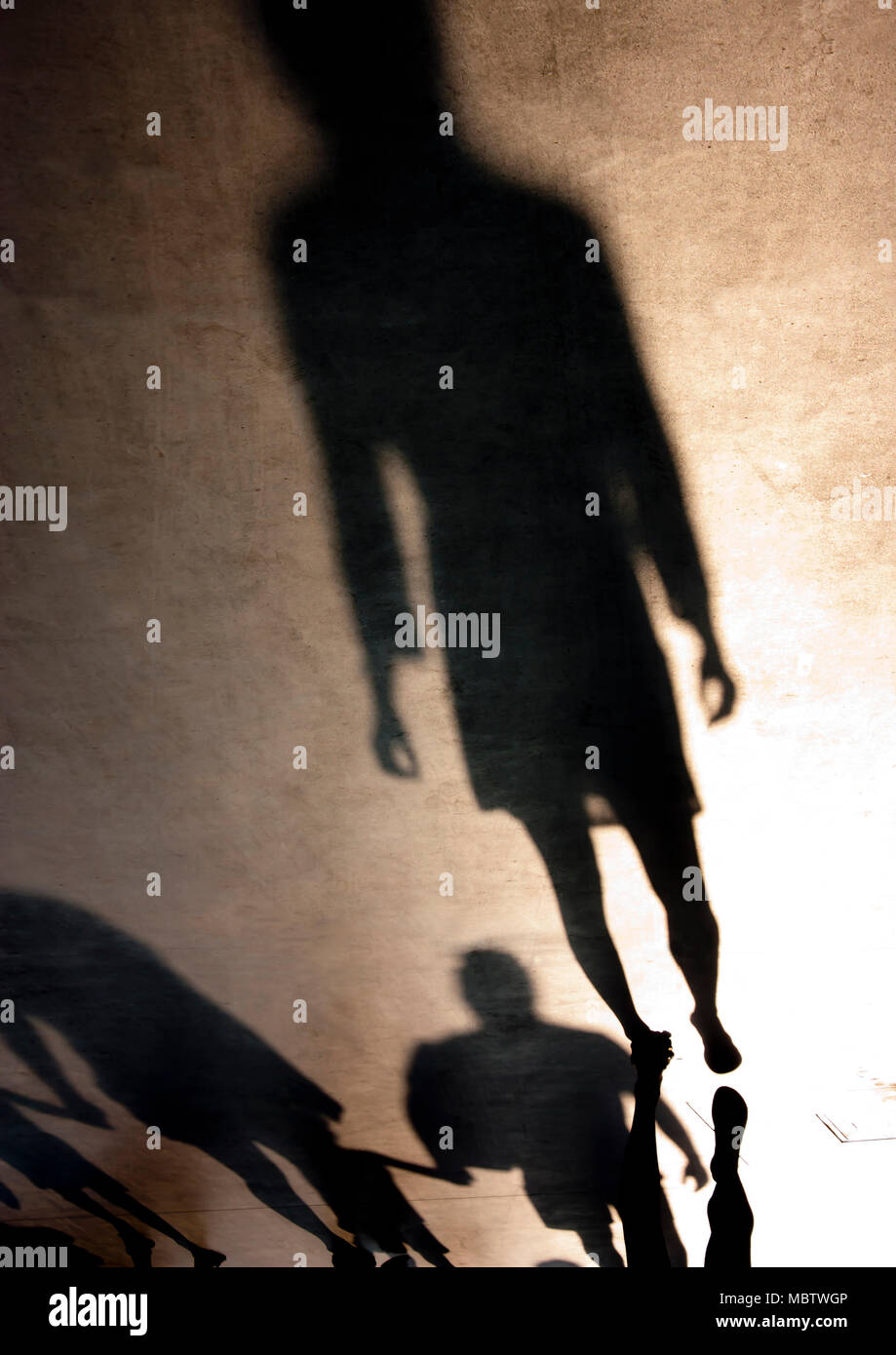 Unscharfe silhouette Schatten der eine junge Frau und ein junger Familien mit Kindern Hand in Hand beim Gehen hinter ihr in sepia schwarz und weiß im Sommer Stockfoto