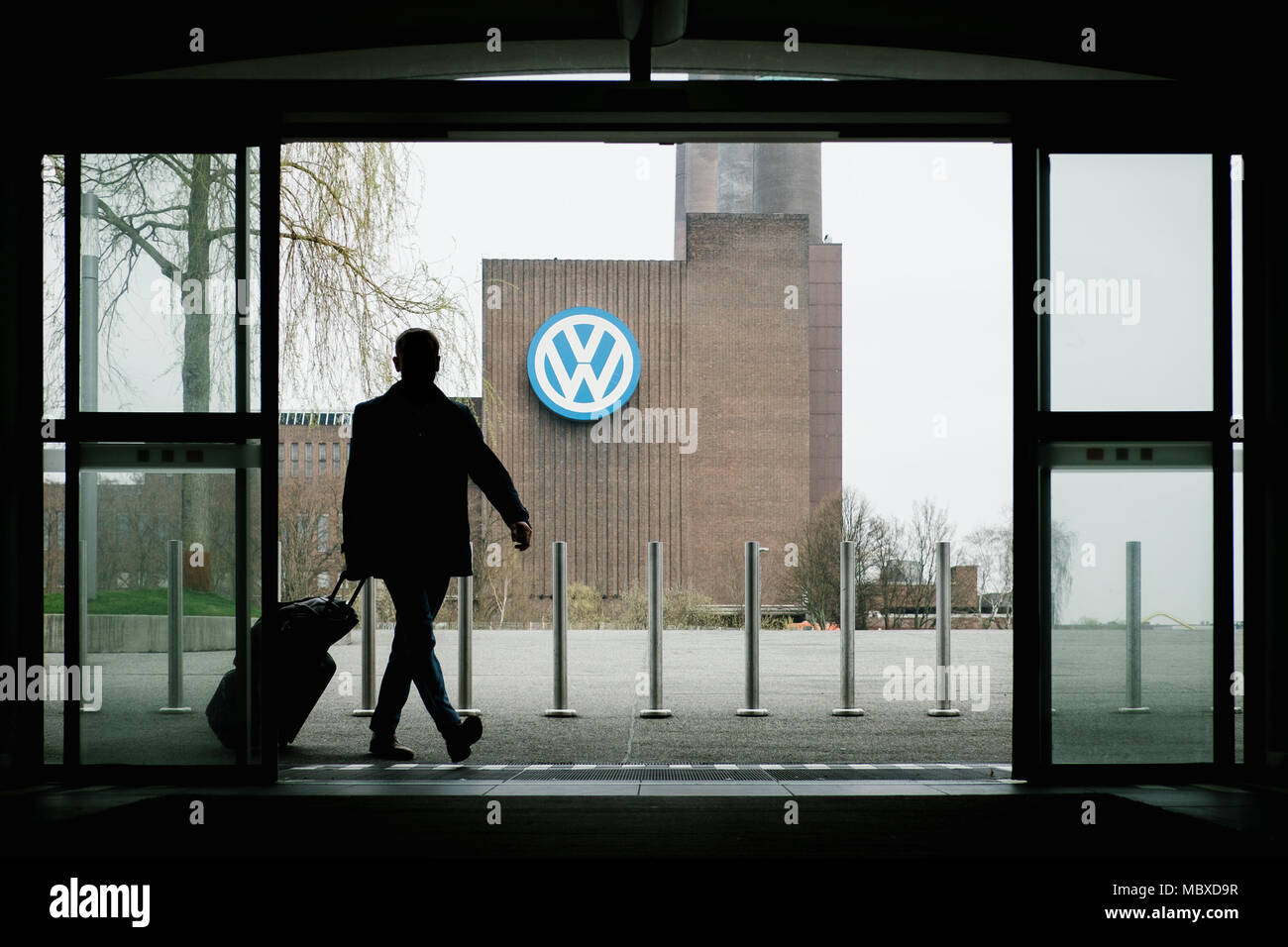 12 April 2018, Deutschland, Wolfsburg: Menschen verlassen Sie den Hauptbahnhof, im Hintergrund taucht das Volkswagen Werk. Der Vorstand der Gesellschaft wird ihre bevorstehende Umstrukturierung diskutieren. Foto: Ole Spata/dpa Stockfoto