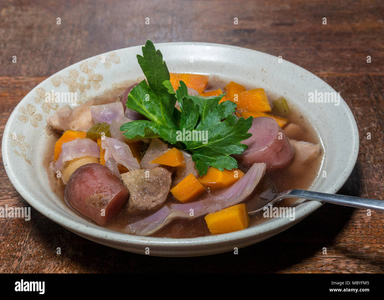 Crockpot Eintopf mit Kartoffeln, Rindfleisch, Rotkraut und Karotten in tan Bogen, garniert mit sellerieblätter, auf Holztisch, vom Dinner Winkel gesehen. Stockfoto