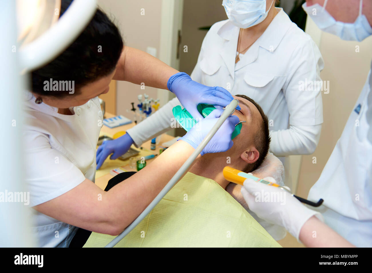 Hände Zahnarzt in blaue Handschuhe mit Ausrüstung in der Nähe des geöffneten Mund eines jungen Mannes. Ein Zahnarzt mit einem fußarzt in der zahnmedizinischen Praxis. Stockfoto