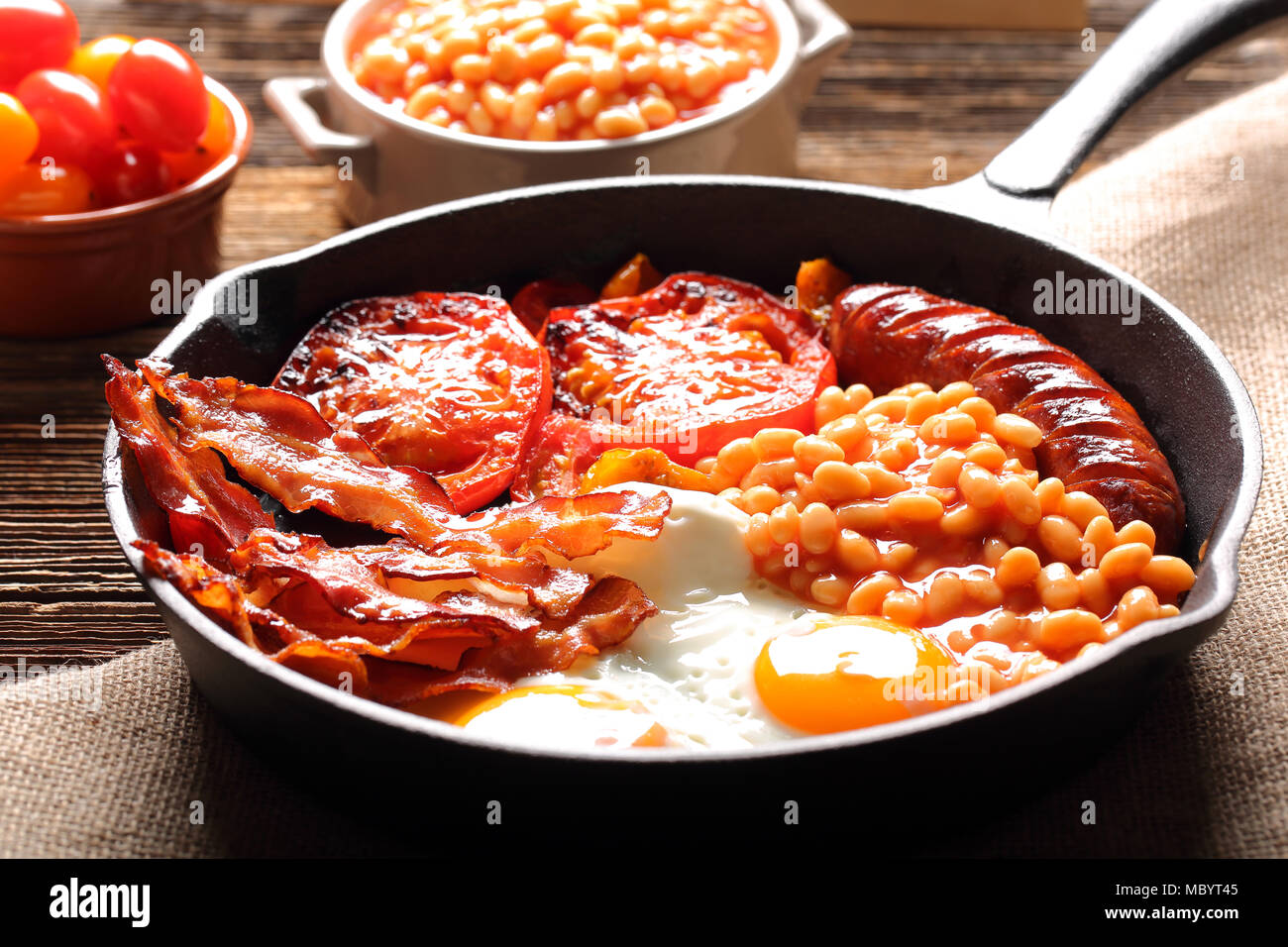 Englisches Frühstück mit Würstchen, gegrillte Tomaten, Eier, Speck und Bohnen auf der Pfanne. Stockfoto
