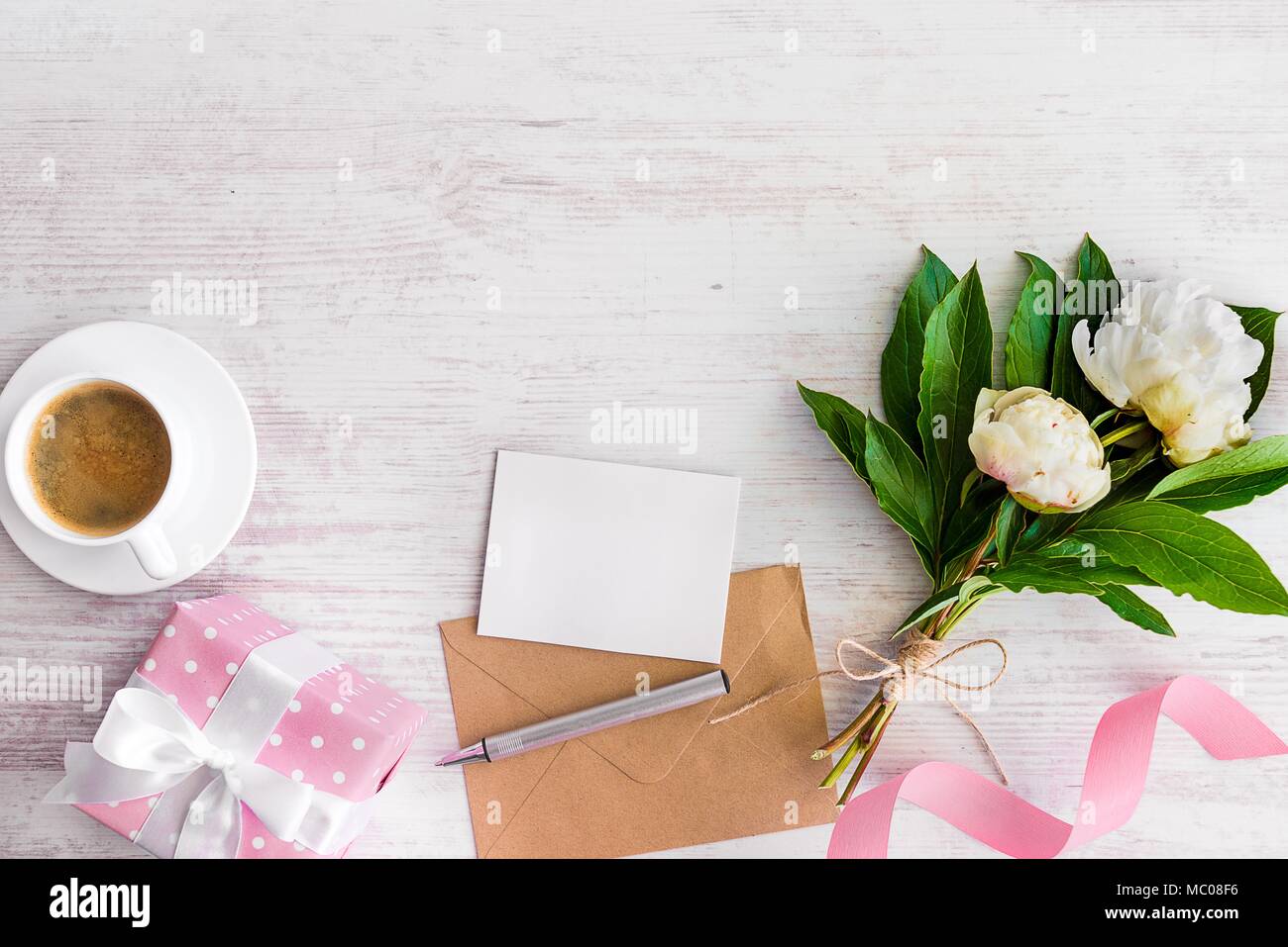 Ansicht von oben Leerer Hinweis, Kraftpapier Umschlag, Kaffeetasse und Pfingstrose Blüten mit weißem Holz rustikale Hintergrund. Platz kopieren. Stockfoto