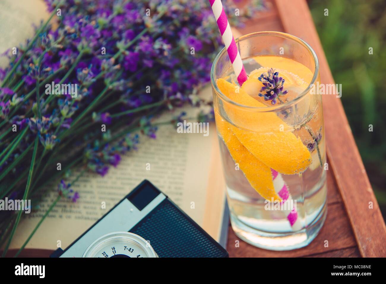 Ein Glas erfrischende Limonade, vintage Cameta, ein Buch und frisch geschnittenen Lavendel Blumen über einen hölzernen Stuhl. Stockfoto