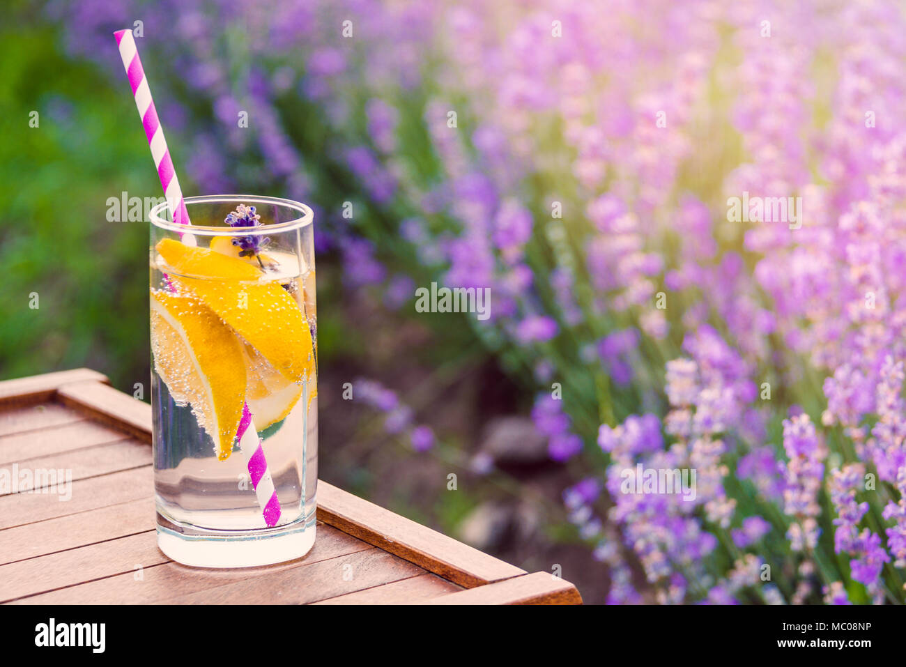 Ein Glas erfrischende Limonade über einen hölzernen Stuhl. Blühende Lavendel Blumen im Hintergrund. Stockfoto