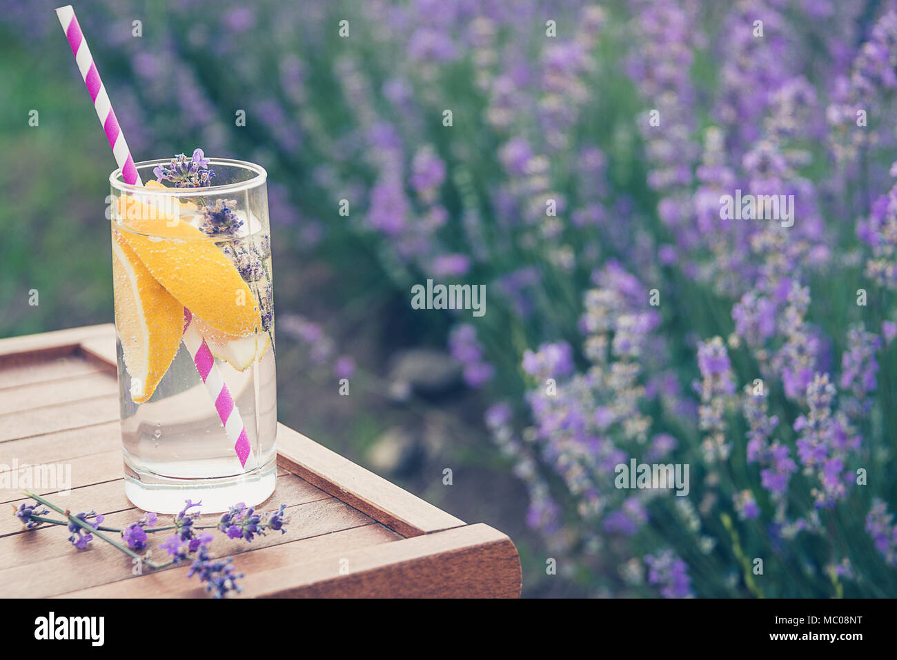 Ein Glas erfrischende Limonade über einen hölzernen Stuhl. Blühende Lavendel Blumen im Hintergrund. Stockfoto