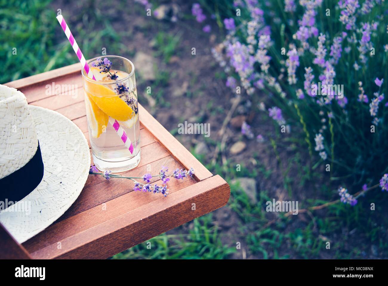 Ein Glas erfrischende Limonade und einen Strohhut über einen hölzernen Stuhl. Blühende Lavendel Blumen im Hintergrund. Stockfoto