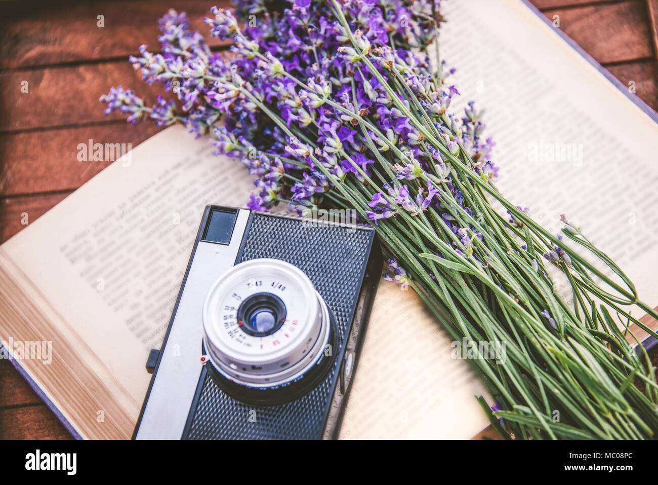 Frisch geschnittenen Lavendel Blumen und ein Vintage Foto Kamera über ein offenes Buch. Holz- Hintergrund Stockfoto