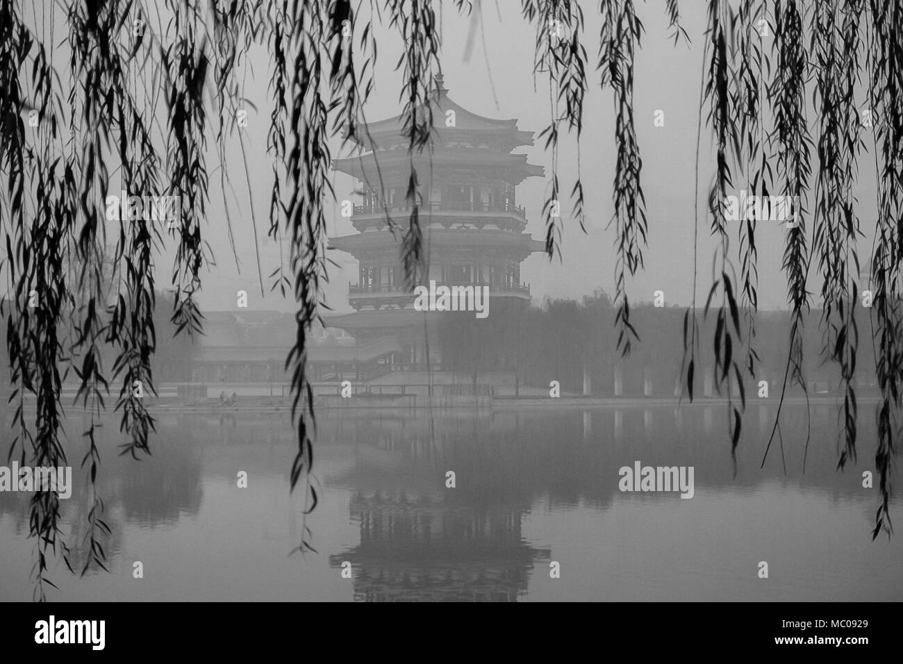 Chinesische Pagode, zentriert und gerahmt, von Trauerweide am Rande eines Sees. Schwarz/Weiß-Bild eines smoggy, grau November Tag, Xi'an, China Stockfoto