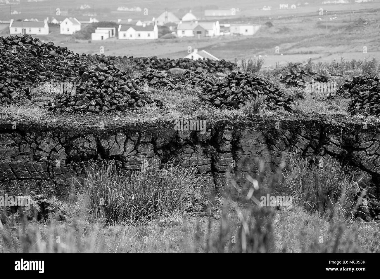 Schwarz und Weiß, Szene von Torf mit Dorf Hintergrund auf Achill Island, County Mayo in Irland. Horizontale einer Torf ausschneiden, mit Torf Stapeln trocknen Stockfoto