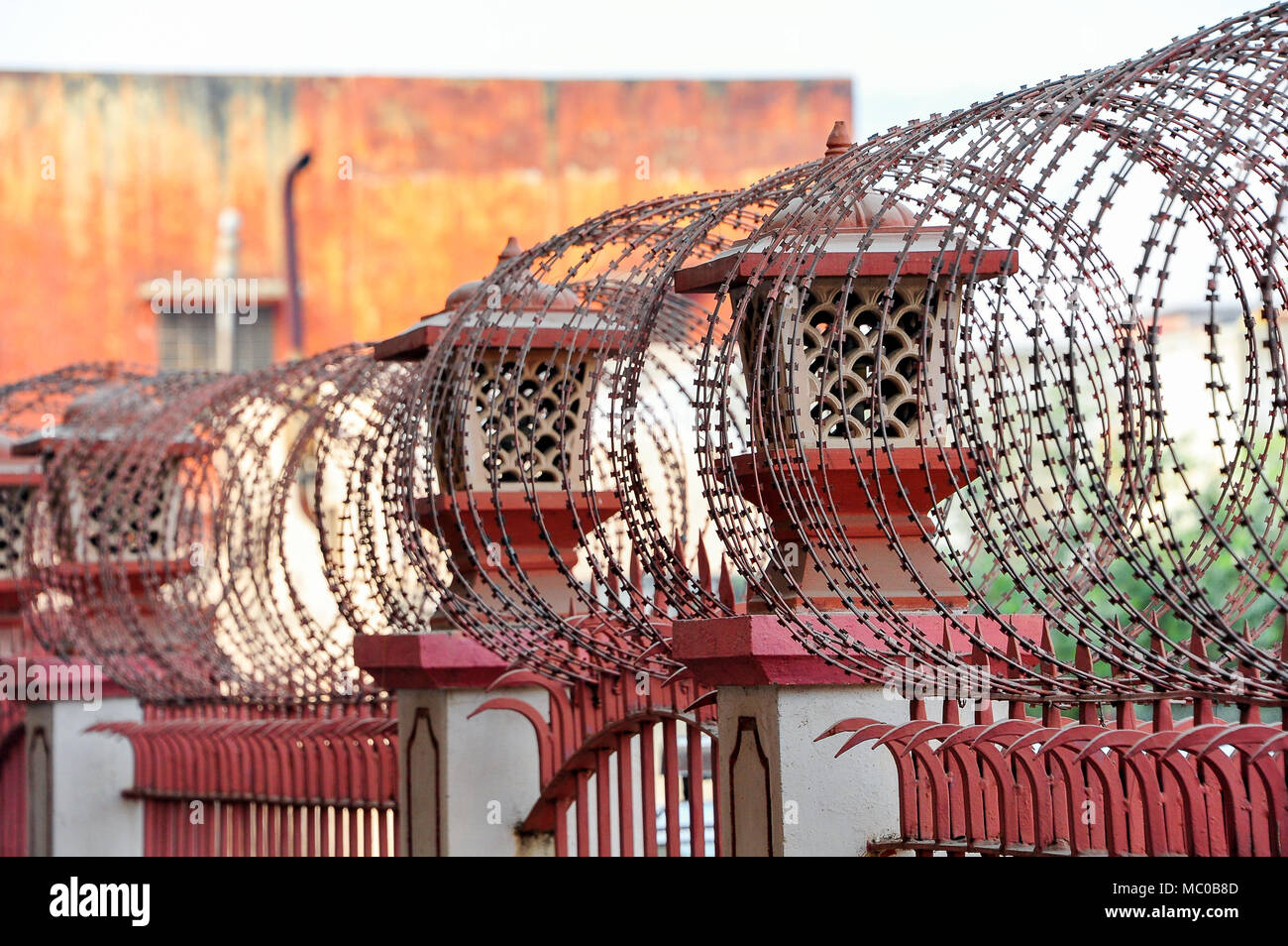Maßnahmen zur Gefahrenabwehr auf der Außenseite eines roten Backsteingebäude in Jaipur, Indien. Stacheldraht auf einem rot lackierten, dekorativen schmiedeeisernen Zaun Stockfoto