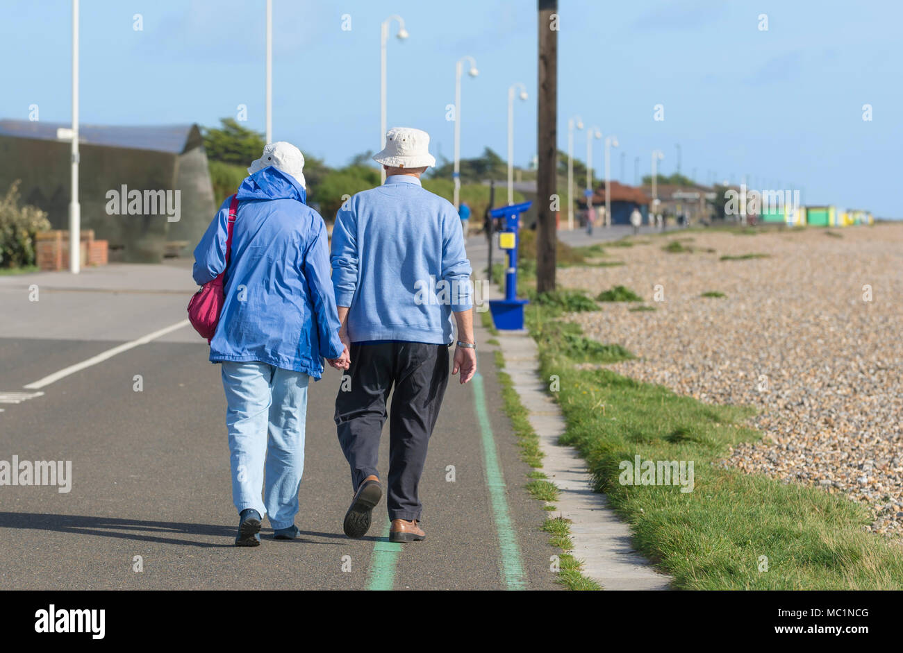 Senior Paar entfernt halten sich an den Händen entlang der Strandpromenade, an einem sonnigen Tag in Littlehampton, West Sussex, England, UK. Direkt am Meer spazieren. Stockfoto