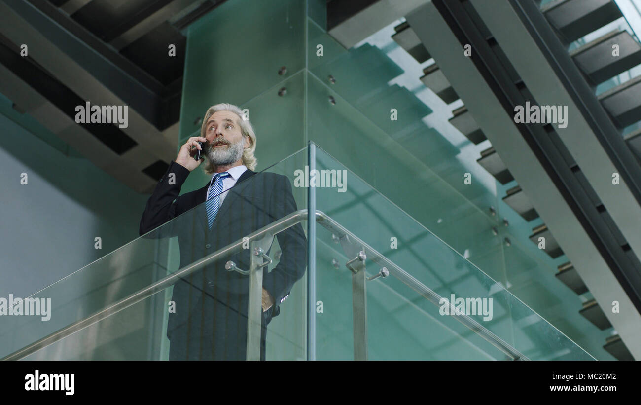 Senior Corporate Executive stehen im zweiten Stock in einem modernen Bürogebäude eine können Sie über Handy anzurufen. Stockfoto